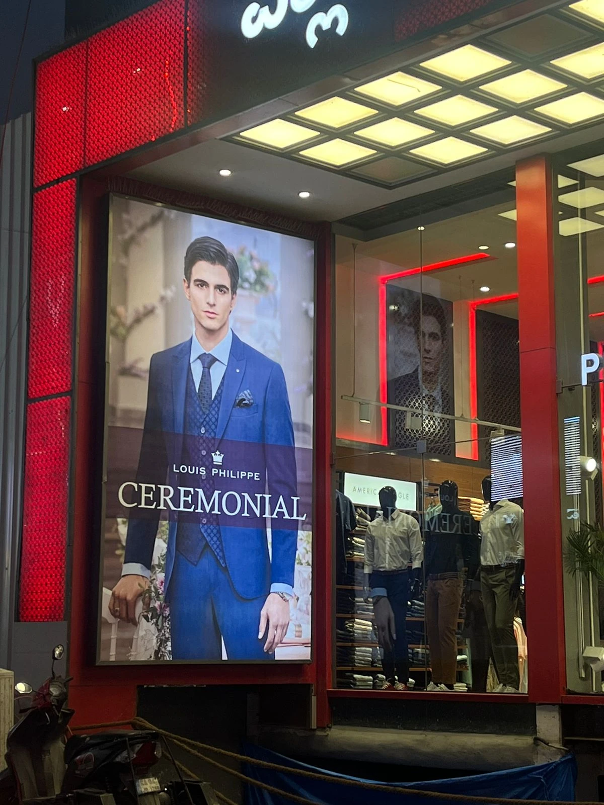 Louis Philippe Ceremonial campaign featuring Luca Bold in a blue three-piece suit, on a lit store-front lightbox in India